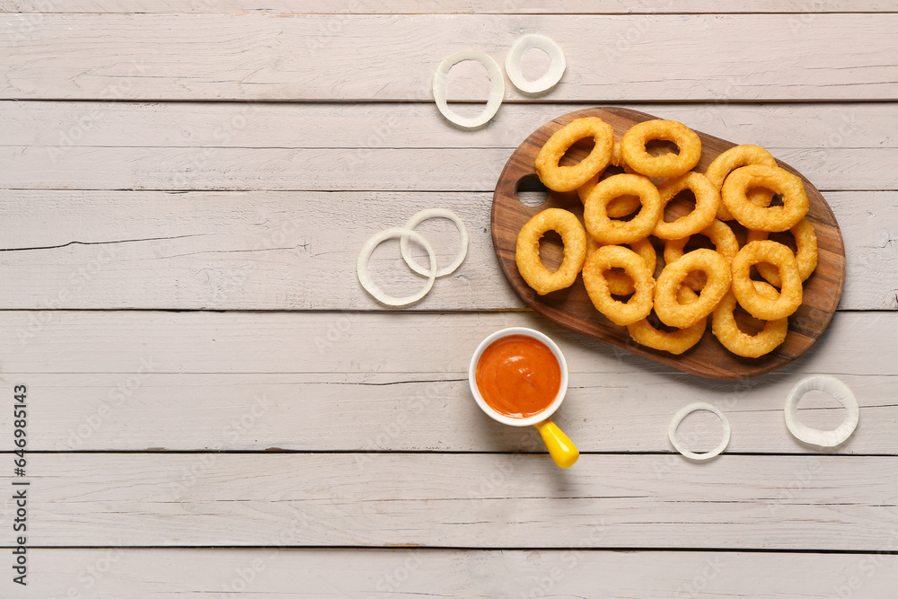 Board with fried breaded onion rings and sauce on grey wooden background