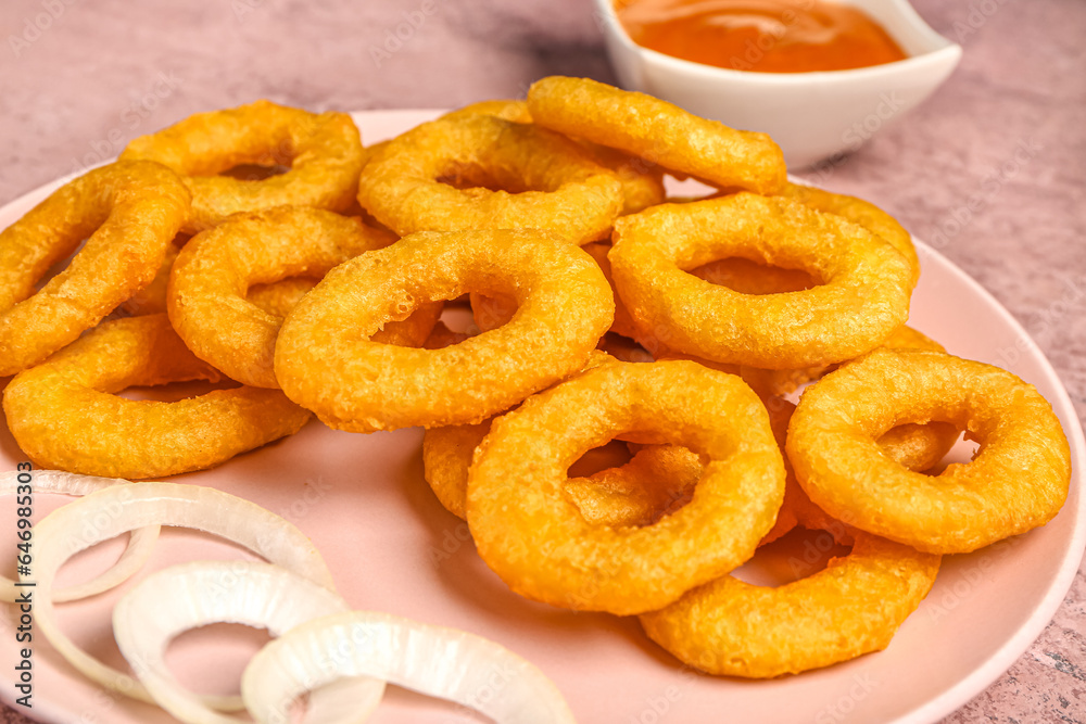 Plate with fried breaded onion rings on pink background, closeup