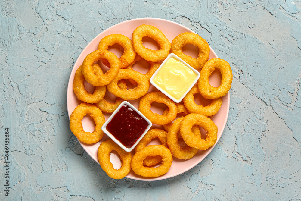 Plate with fried breaded onion rings and different sauces on blue background