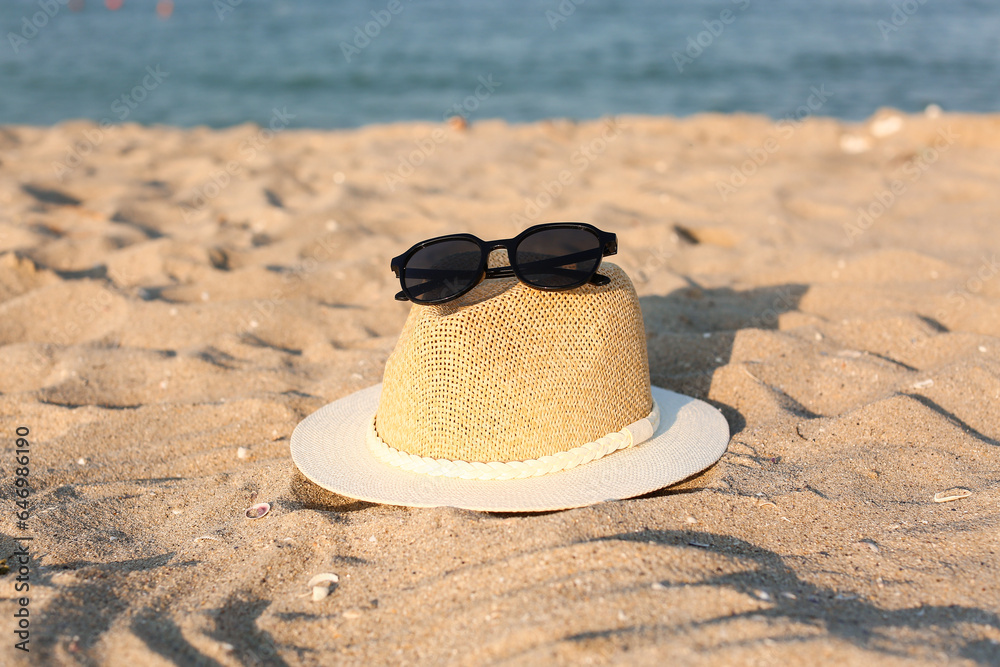 Stylish black sunglasses and hat on seashore