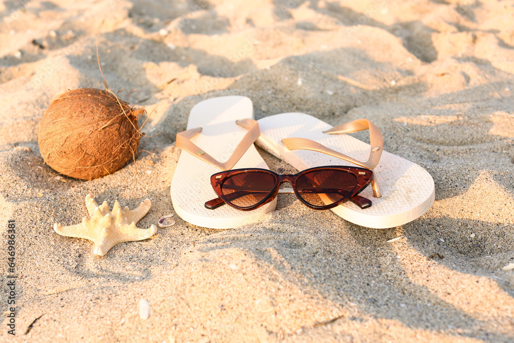 Stylish brown sunglasses with flip flops, starfish and coconut on sand