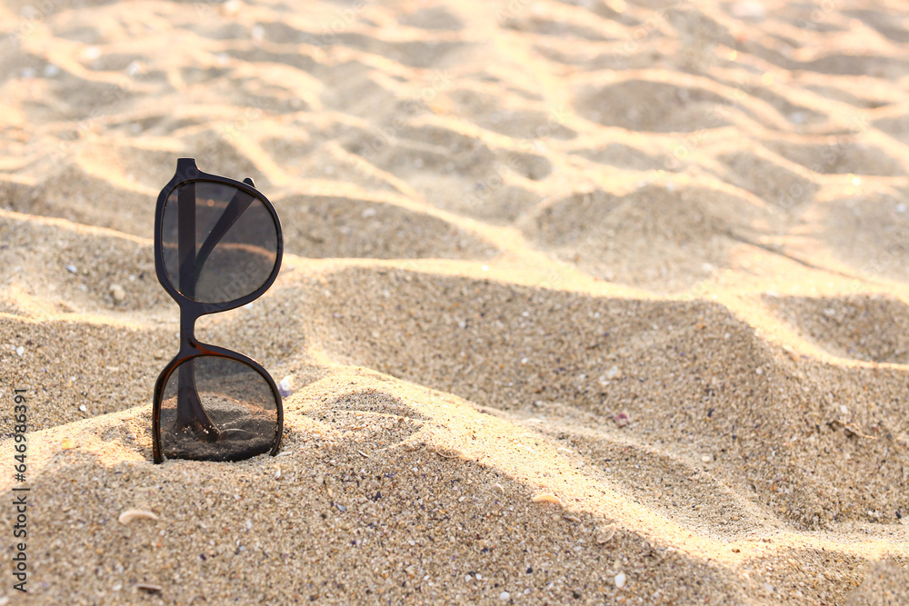 Stylish black sunglasses on sand