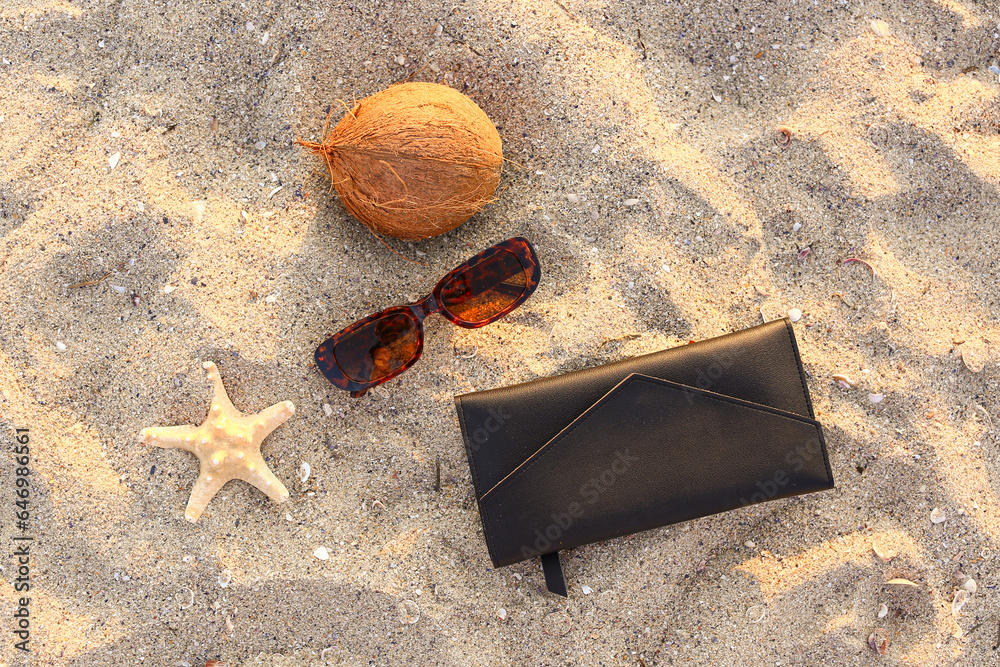 Stylish brown sunglasses with bag, starfish and coconut on sand