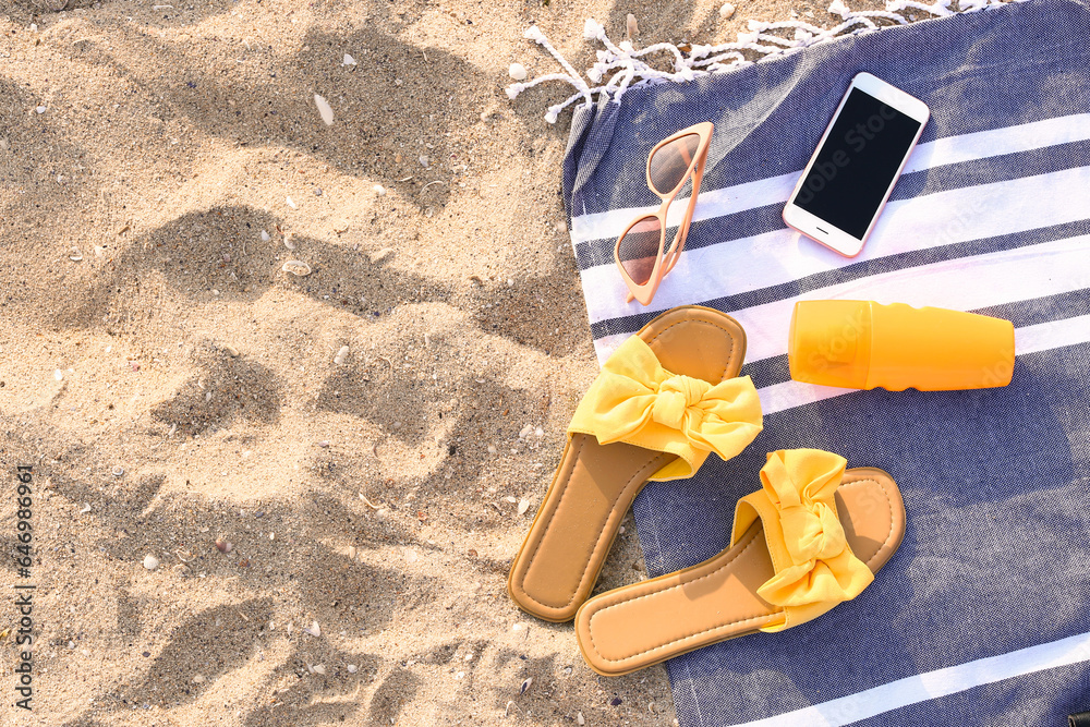 Stylish sunglasses with phone and beach accessories on sandy background