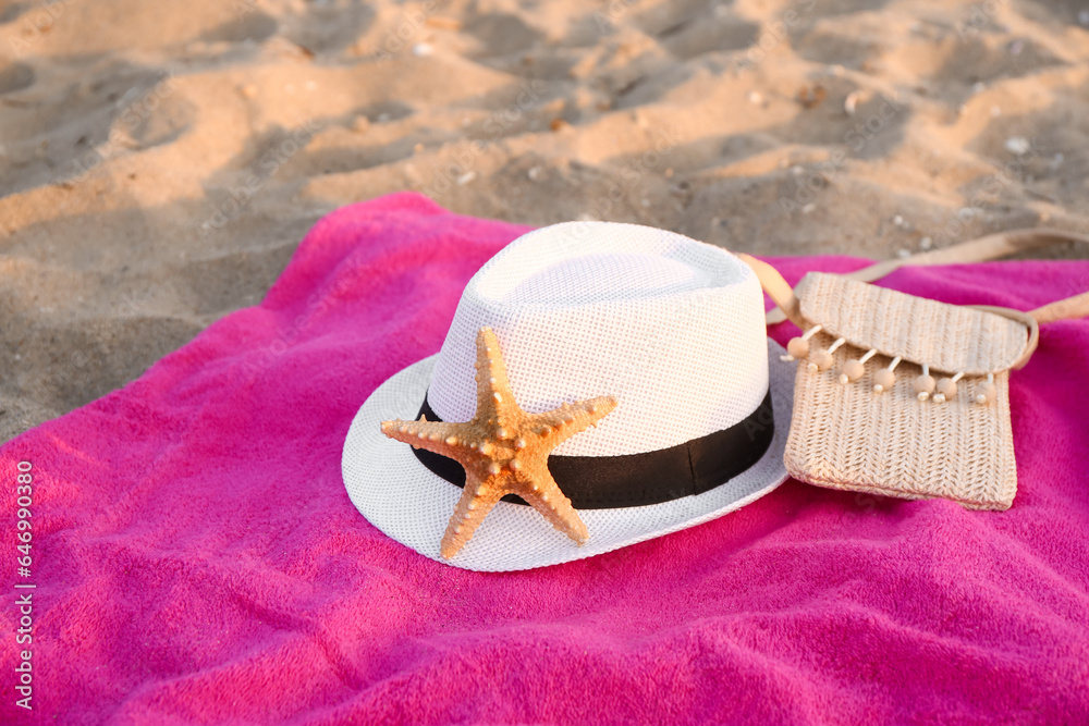 Towel with straw hat, bag and starfish on sand