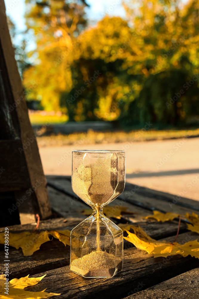 Hourglass with fallen leaves on bench in park, closeup