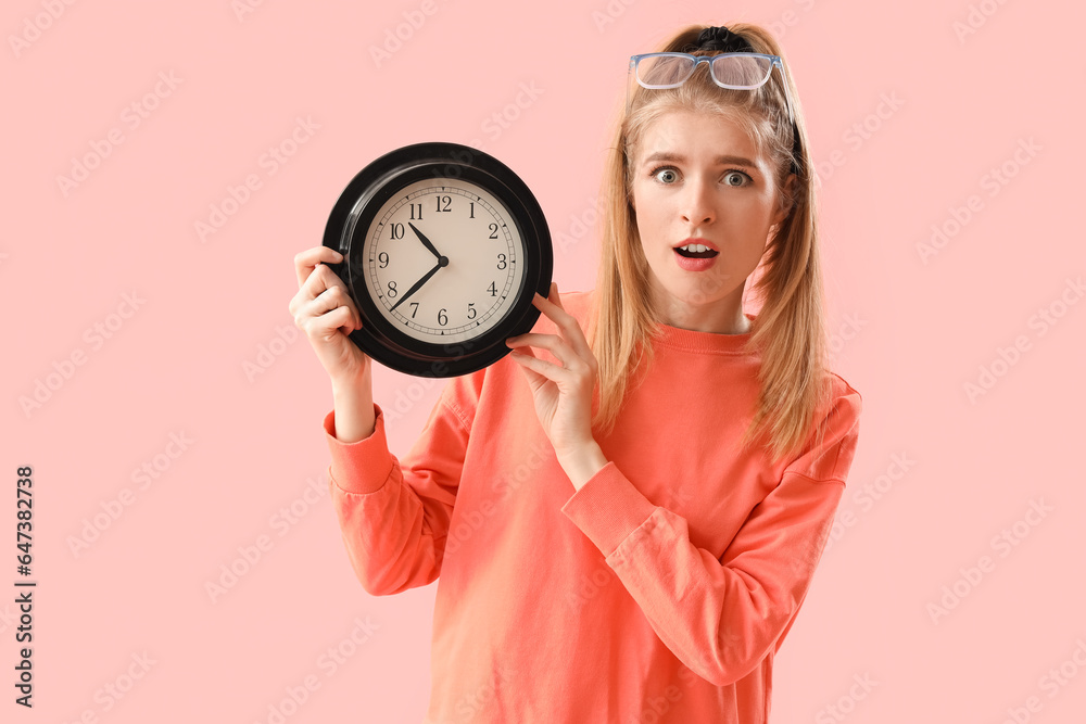 Stressed young woman with clock on pink background. Deadline concept