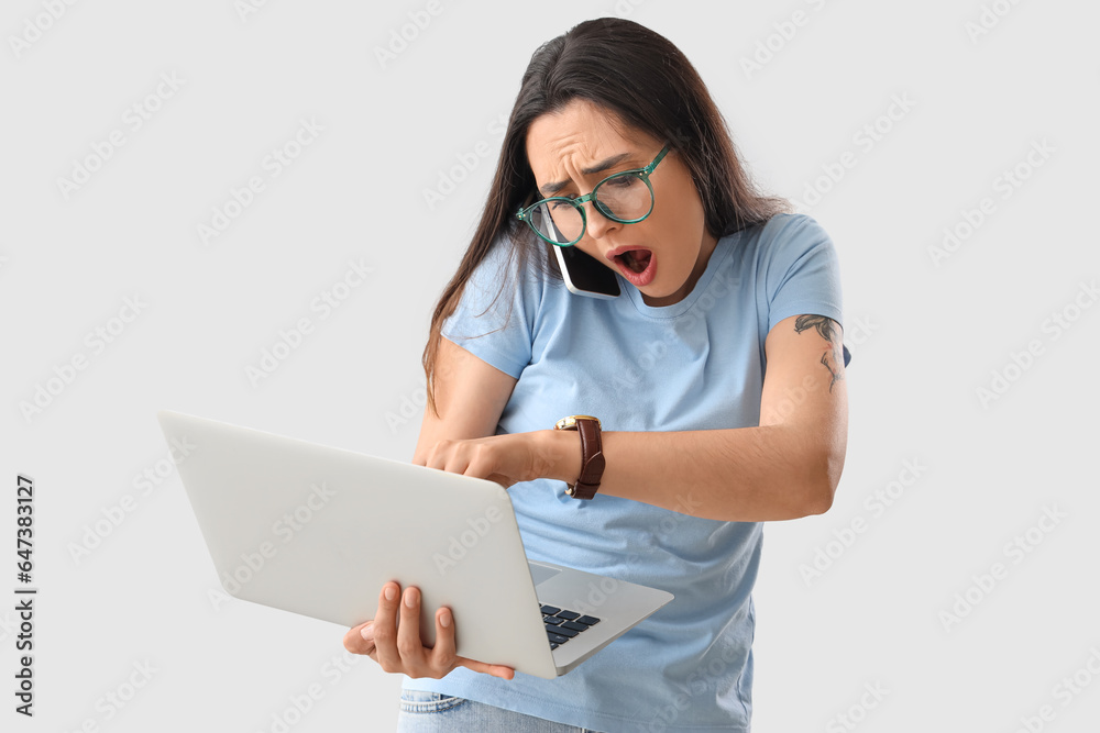 Stressed young woman with wristwatch and laptop talking by mobile phone on light background. Deadlin