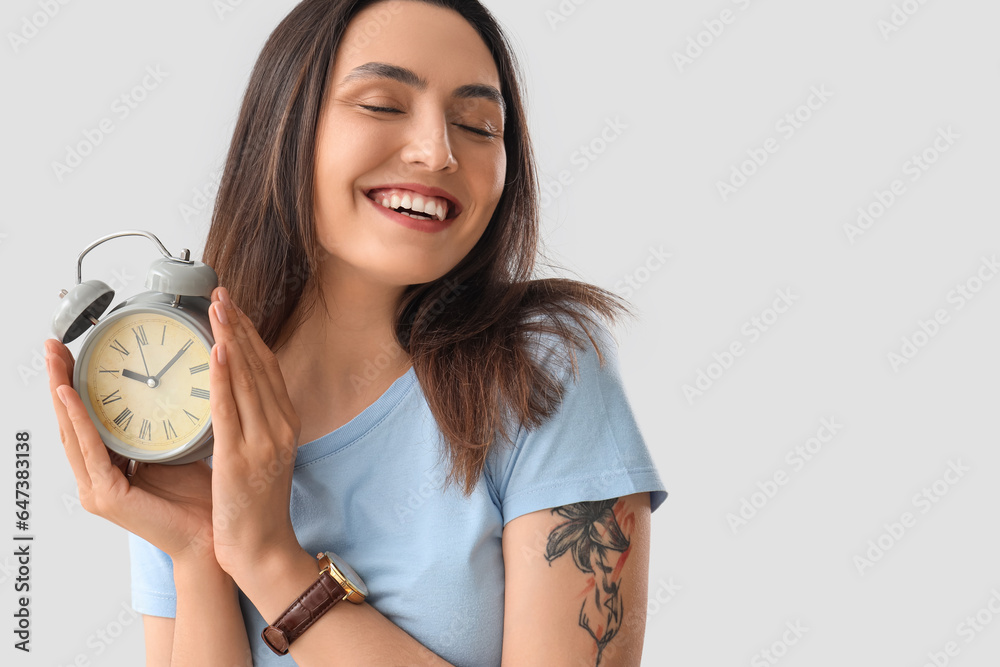 Young woman with alarm clock on light background, closeup. Deadline concept