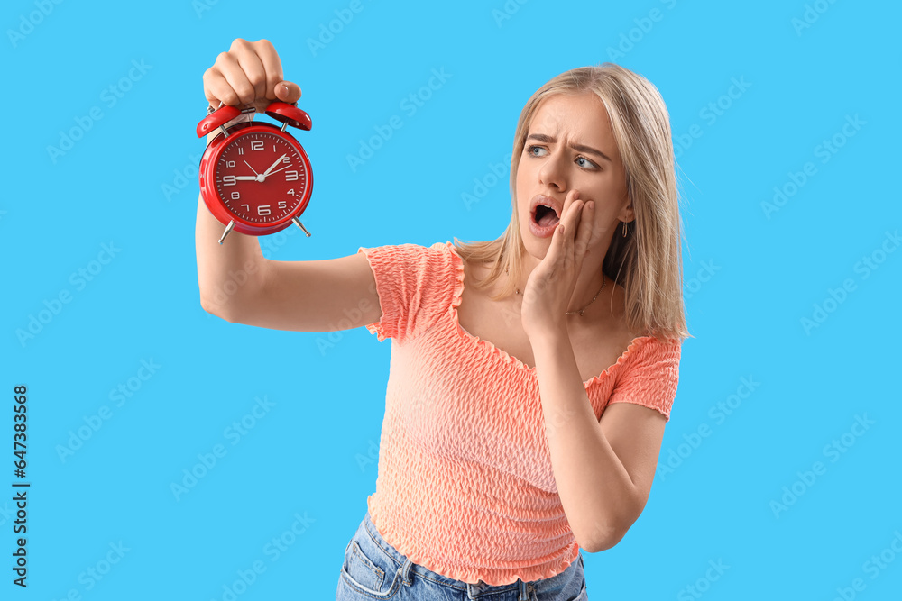 Shocked young woman with alarm clock on blue background. Deadline concept