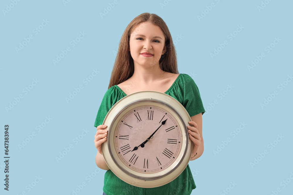 Young woman with clock on blue background. Deadline concept