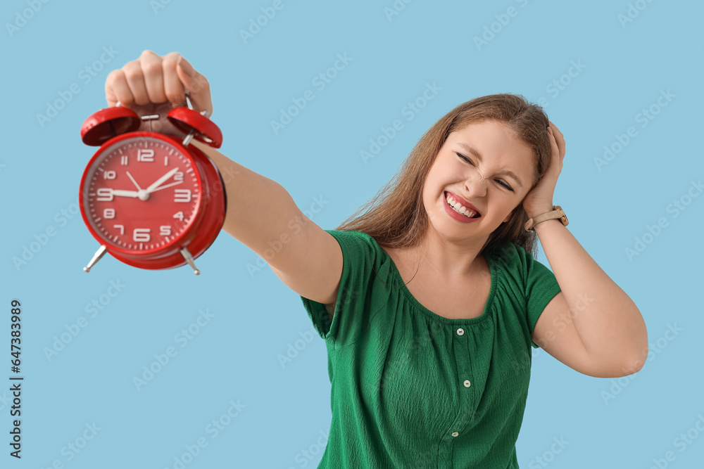 Stressed young woman with alarm clock on blue background. Deadline concept