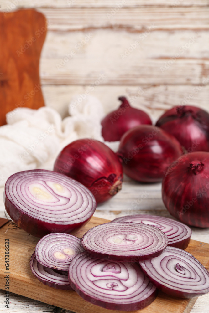 Board with slices of fresh red onion on white wooden background