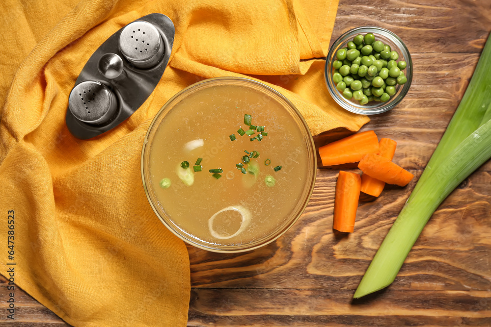 Bowl of tasty vegetable broth and ingredients on wooden background