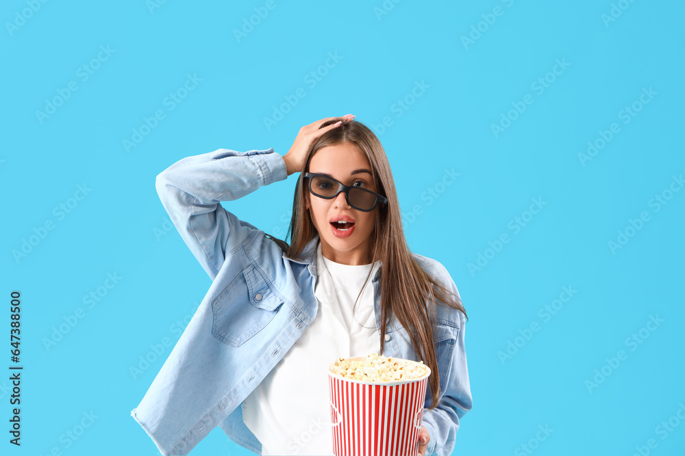 Shocked young woman in 3D glasses with popcorn watching movie on blue background