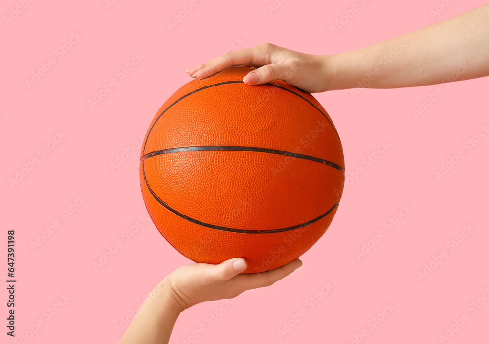 Female hand holding ball for playing basketball on pink background