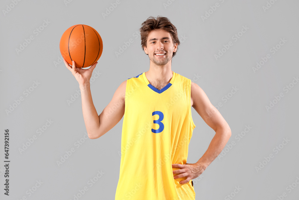 Portrait of young basketball player in yellow uniform holding ball on grey background