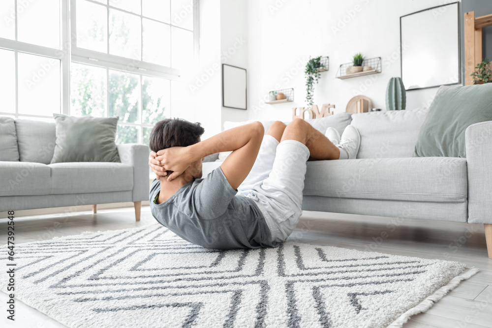 Handsome young man in sportswear swings press at home