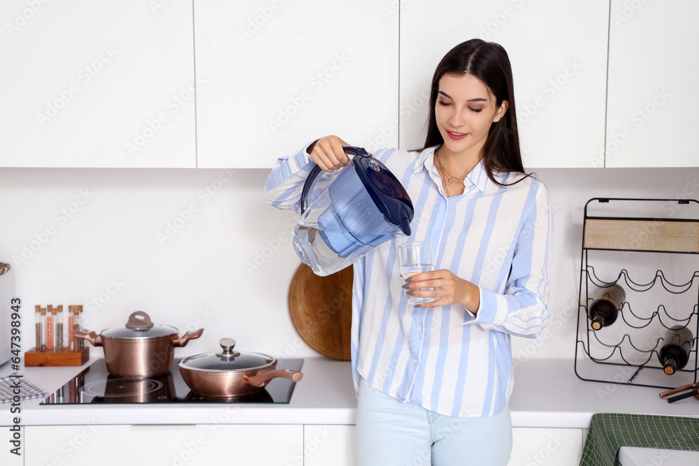 Young woman pouring water from filter jug into glass in kitchen