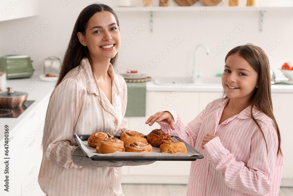 Happy mother with her little daughter and tasty buns in kitchen