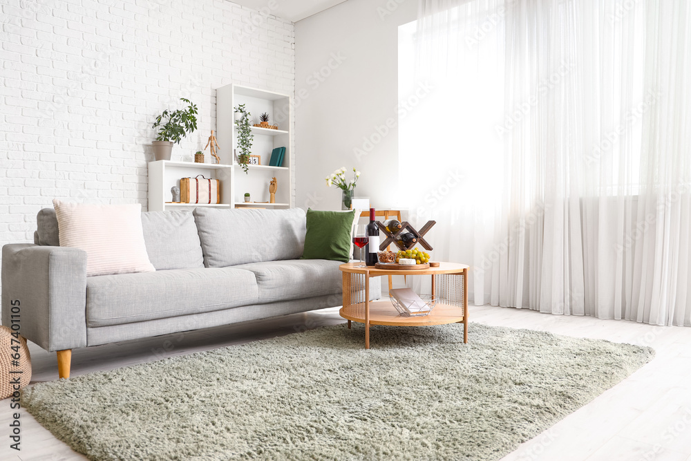 Stylish living room interior with stand of wine bottles and snacks on table