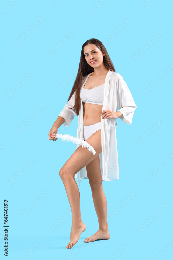 Beautiful young woman with soft feather on blue background. Epilation concept