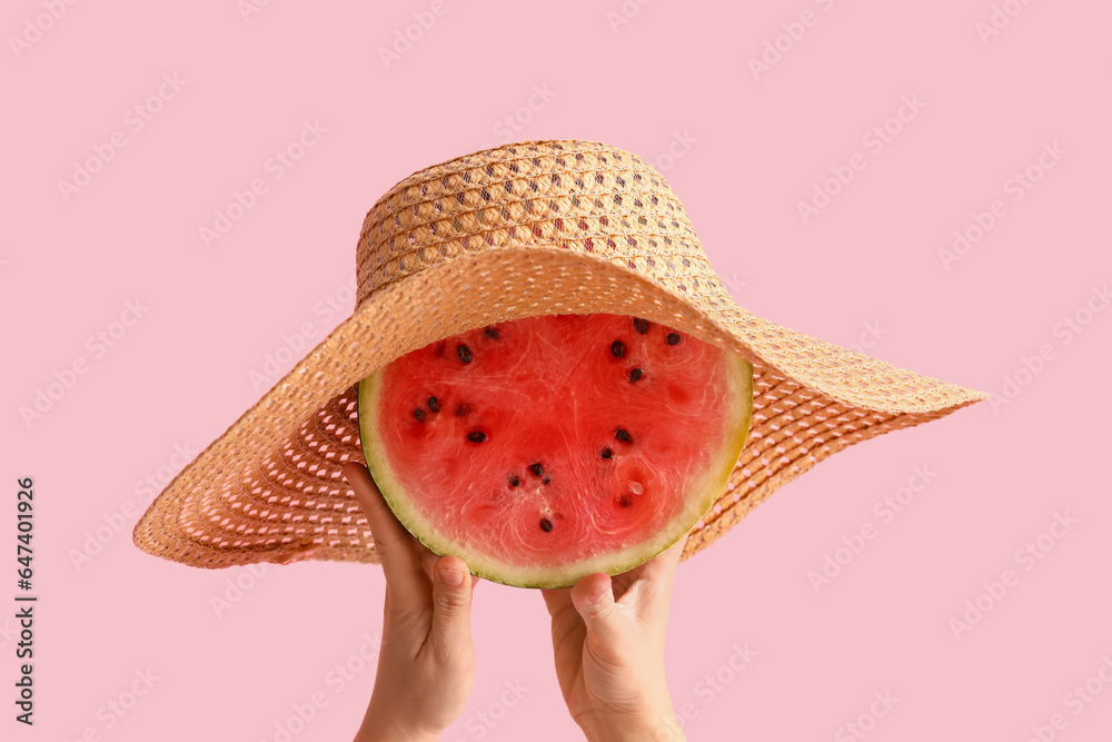 Female hands with slice of fresh watermelon and wicker hat on pink background