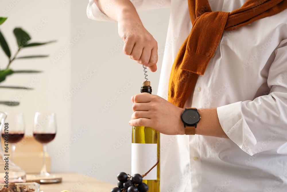 Young sommelier opening bottle of wine in kitchen at home