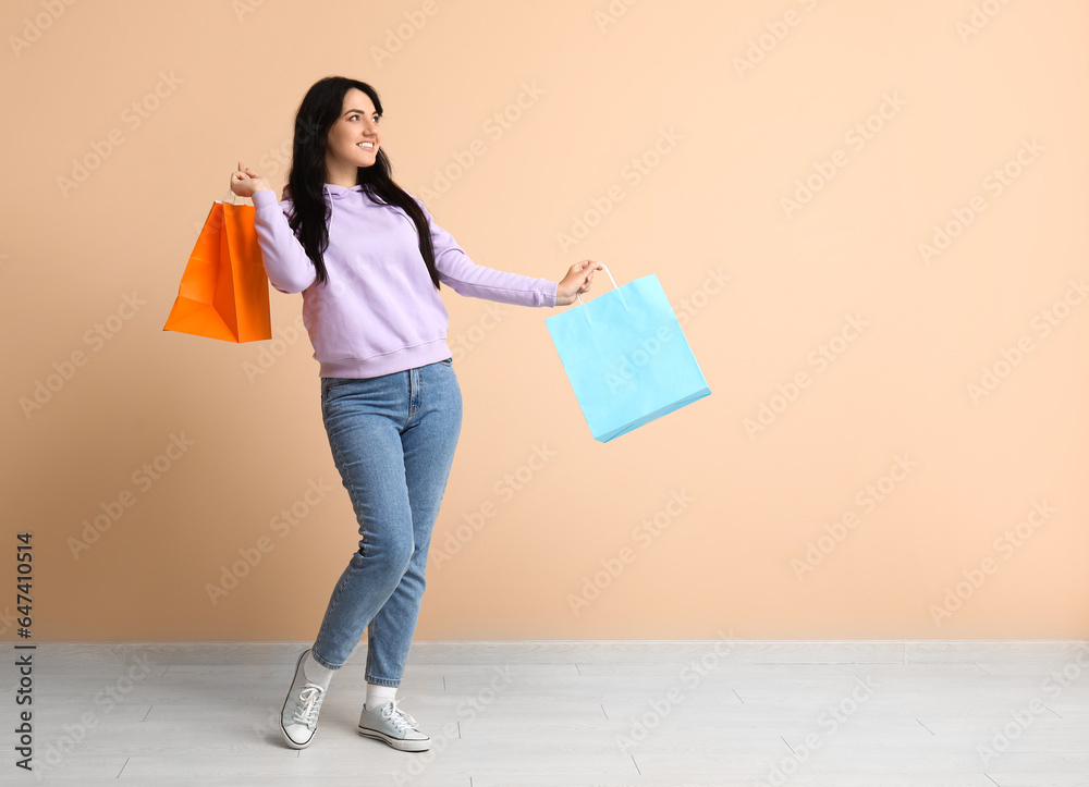 Beautiful happy woman with shopping bags on beige background