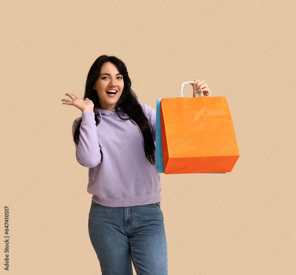 Beautiful happy woman with shopping bags on beige background