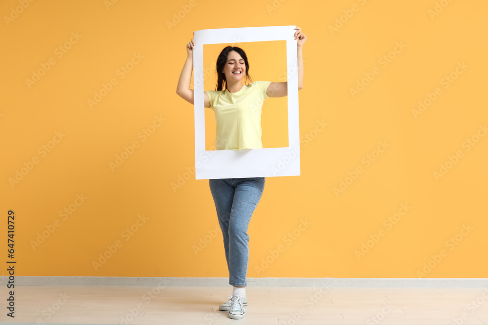 Portrait of happy young brunette with frame on yellow background