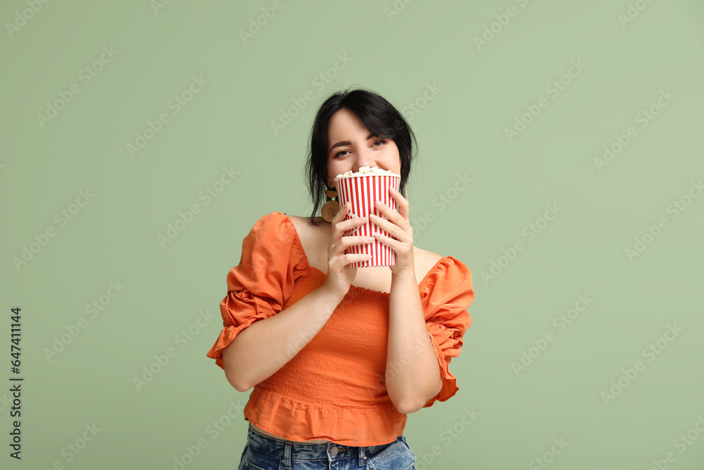 Happy young woman with bucket of popcorn on green background