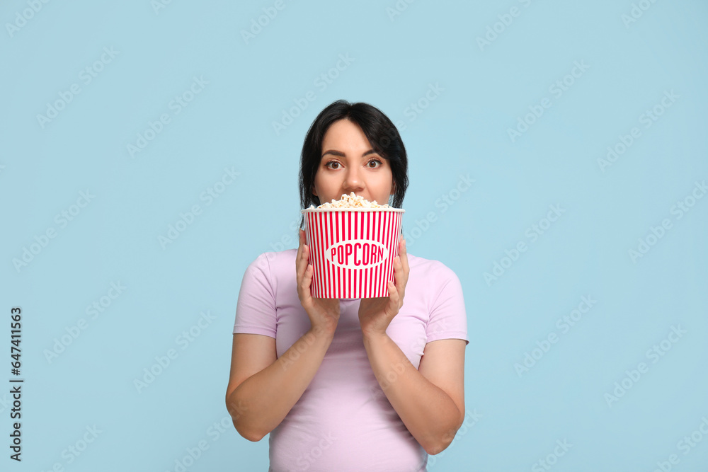 Surprised young woman with bucket of popcorn on blue background