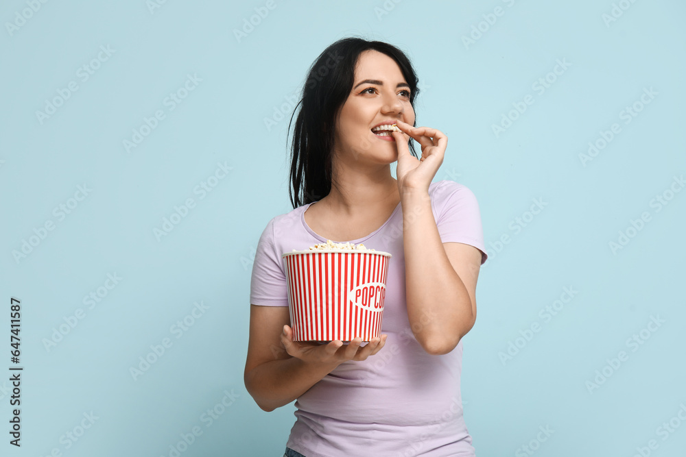 Happy young woman with bucket of popcorn on blue background