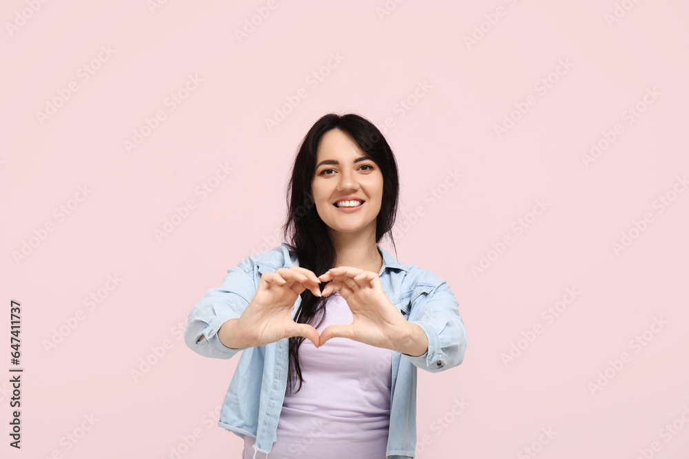 Happy young woman making heart with her hands on pink background