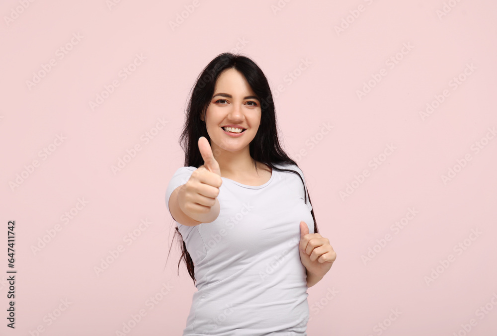 Portrait of happy young brunette showing thumb-up on pink background