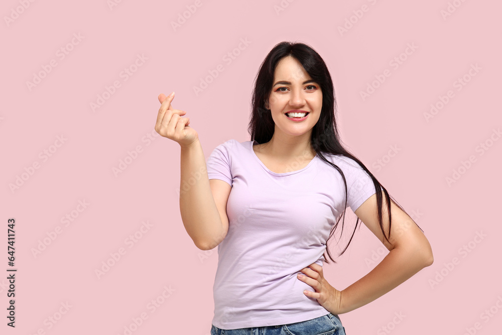 Happy young woman making heart with her fingers on pink background