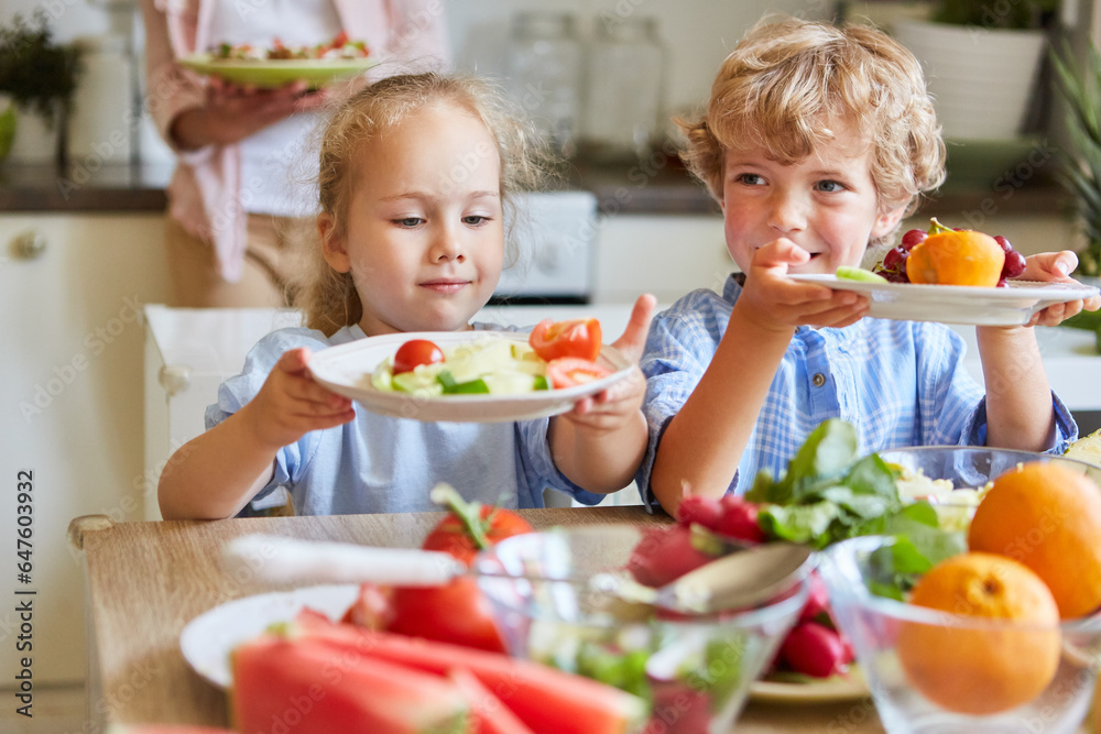 Siblings holding salad plates in kitchen at home