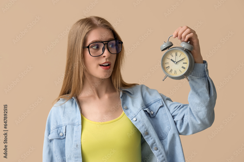 Young woman with alarm clock on beige background. Deadline concept