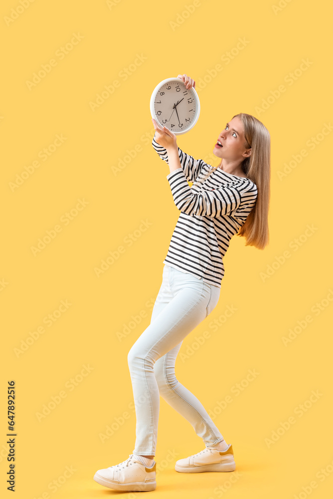 Stressed young woman with clock on yellow background. Deadline concept