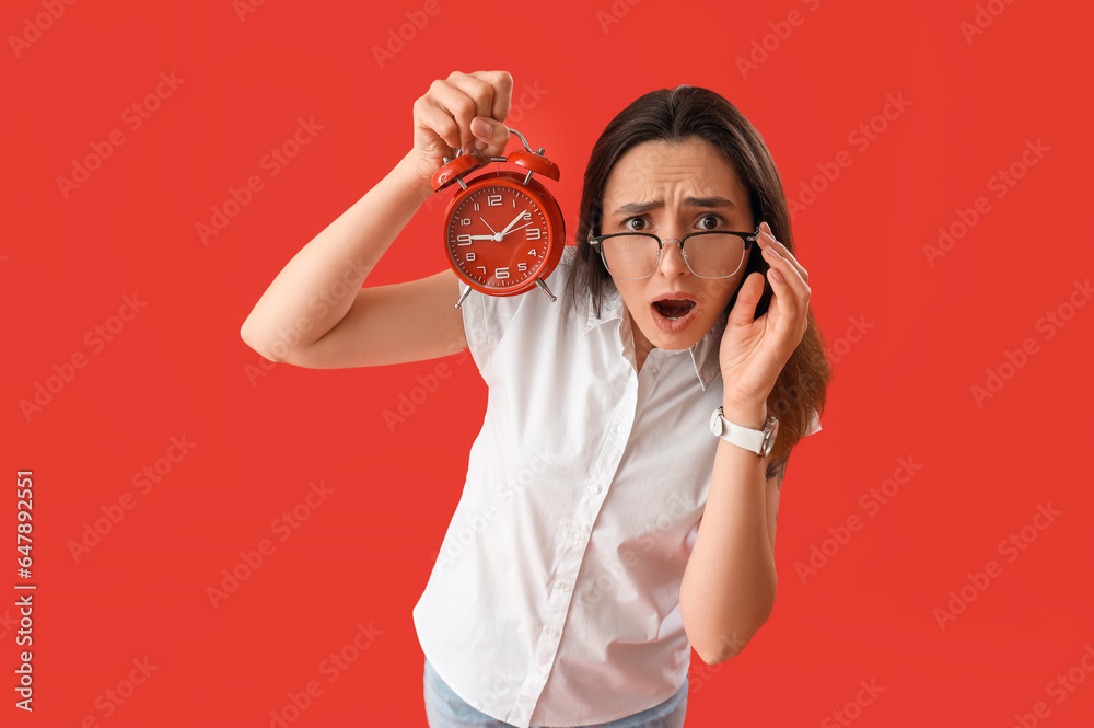 Stressed young woman with alarm clock on red background. Deadline concept