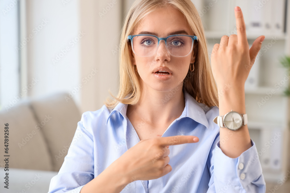 Young businesswoman pointing at wristwatch in office. Deadline concept