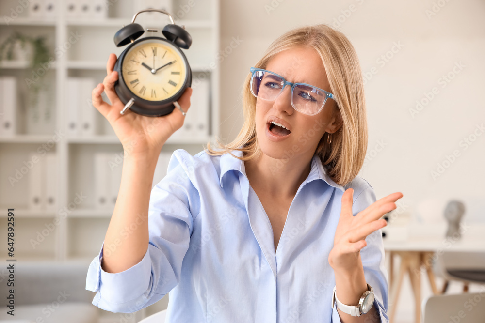 Stressed young businesswoman with alarm clock working under deadline in office, closeup