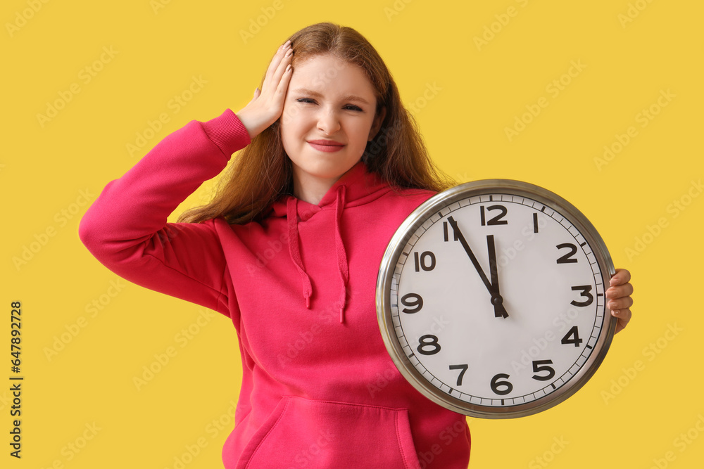 Stressed young woman with clock on yellow background. Deadline concept