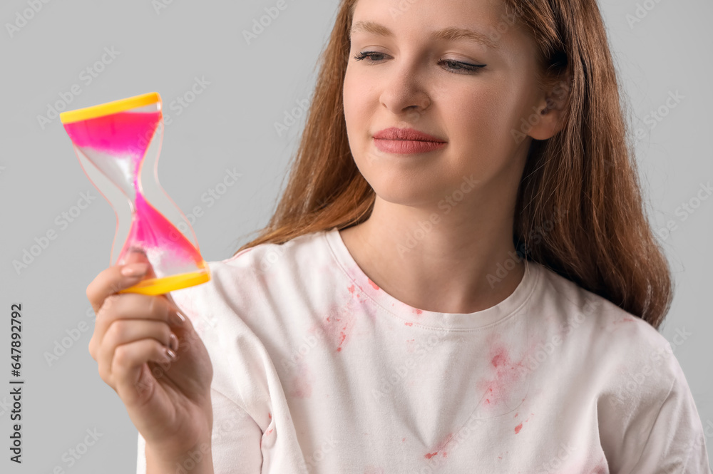 Young woman with hourglass on grey background, closeup. Deadline concept