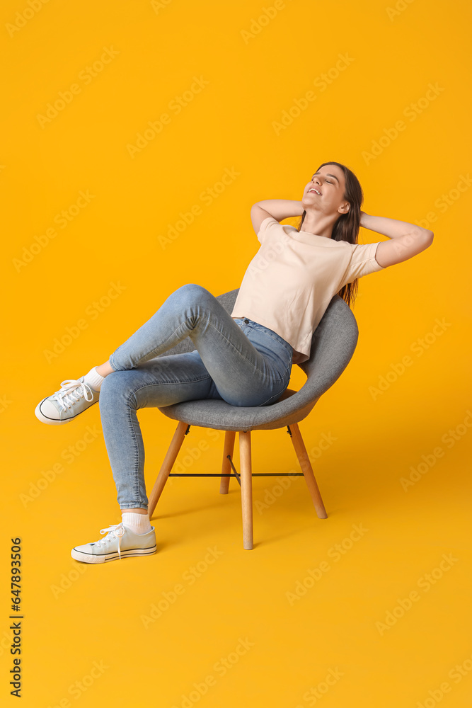 Young woman sitting in armchair on yellow background