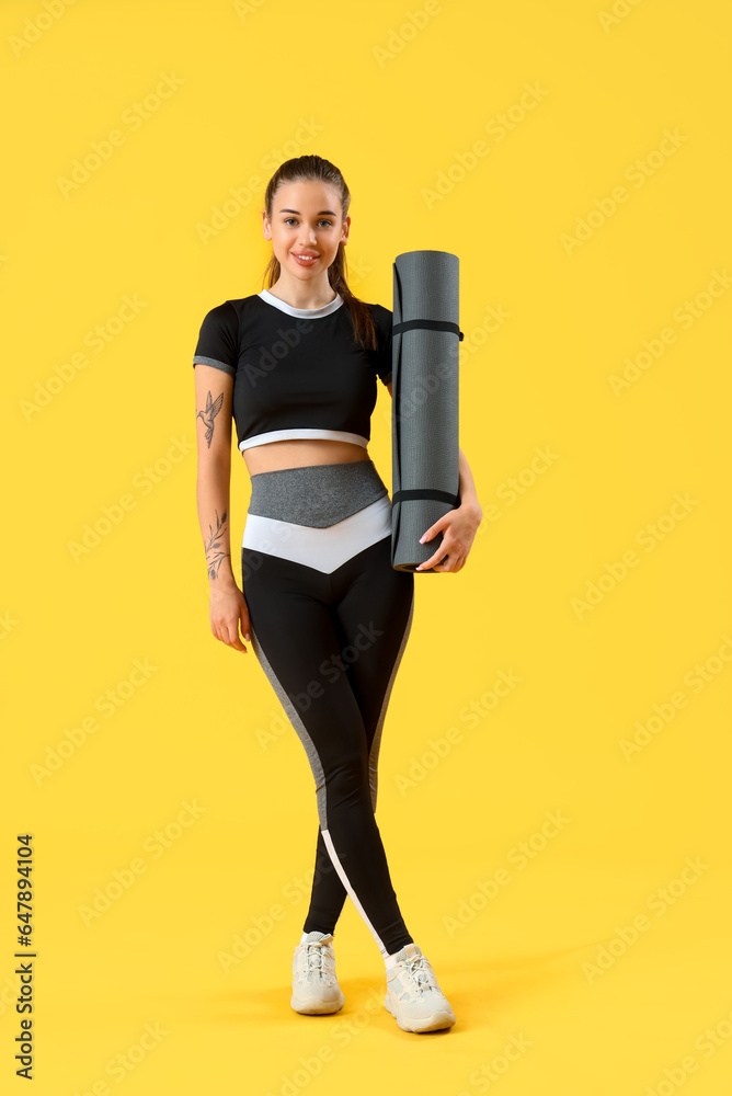 Sporty young woman with fitness mat on yellow background