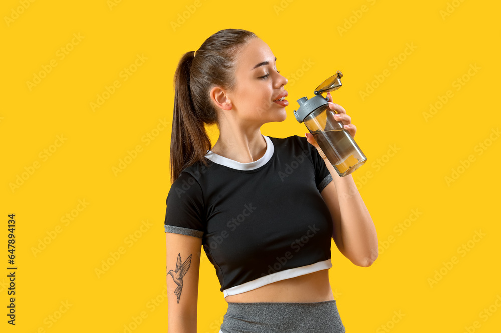 Sporty young woman with bottle of water on yellow background