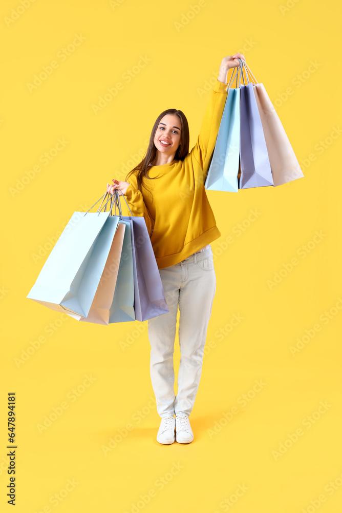 Happy young woman with shopping bags on yellow background