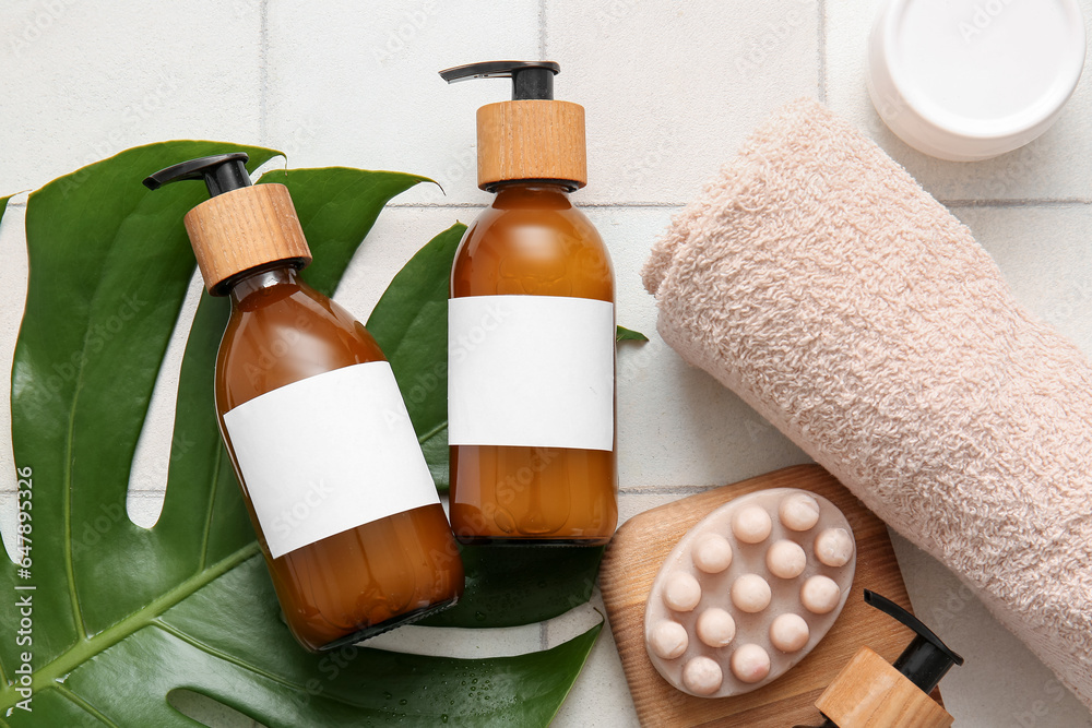 Bottles of shampoo and bath accessories on white tile background